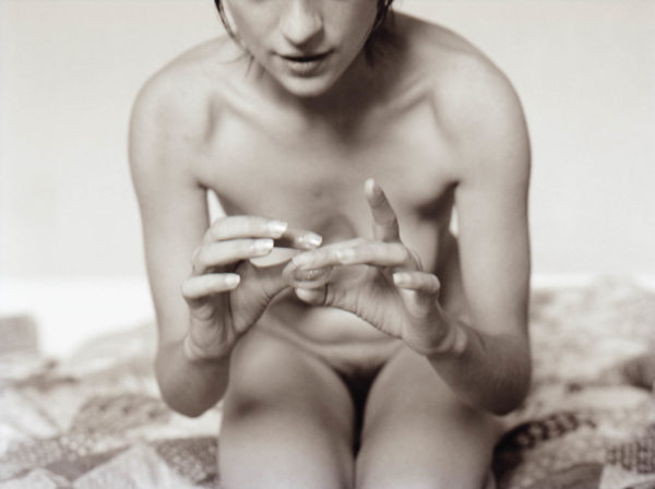 Photographie d'une fille nue avec un préservatif entre ses mains.
