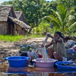 Photographie de Madagascar. Canal des Panglanes. Jeune fille essore la lessive dans de grandes bassines bleues et roses.
