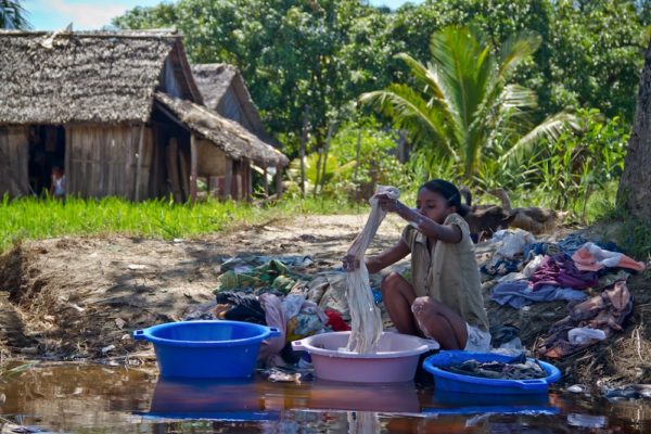 Photographie de Madagascar. Canal des Panglanes. Jeune fille essore la lessive dans de grandes bassines bleues et roses.